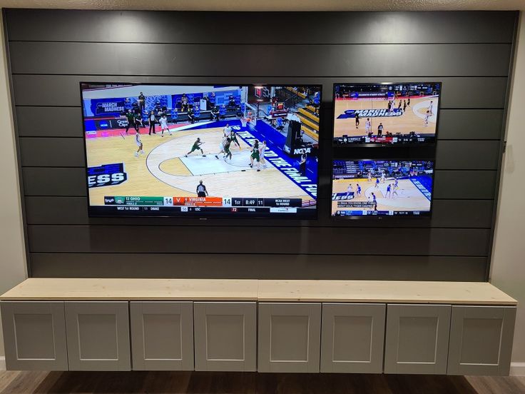 two large televisions mounted on the wall above a bench in a basketball game room