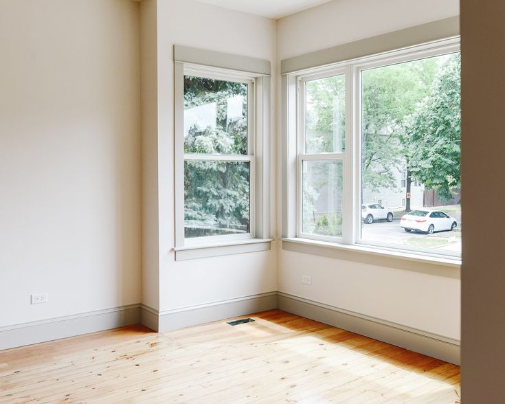 an empty room with two windows and hard wood flooring on one side, looking out onto the street