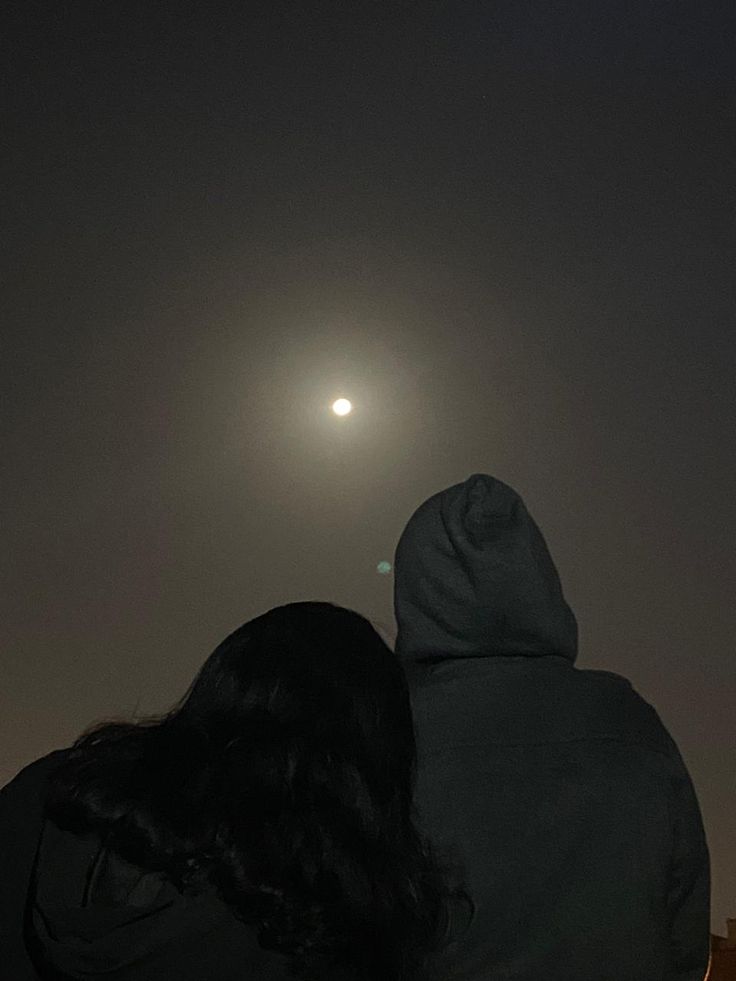 two people are looking at the moon in the sky