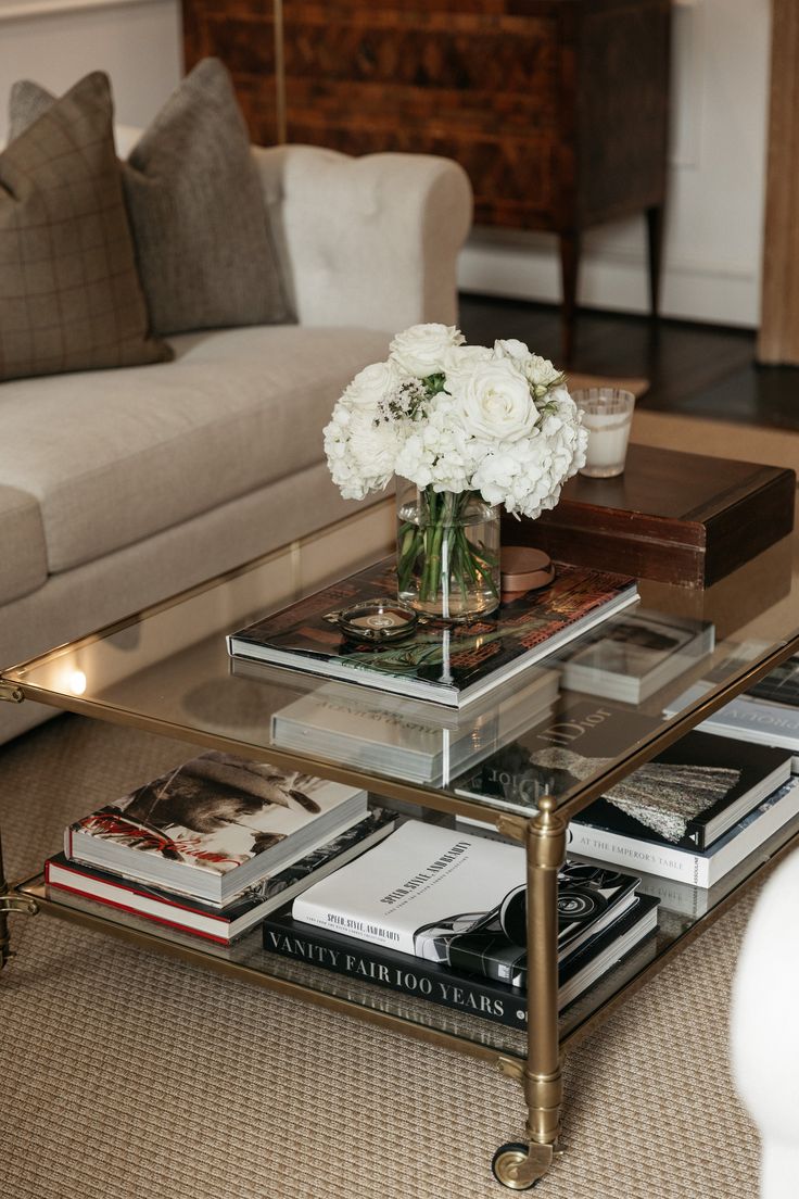 a living room with a couch and coffee table filled with books, flowers and magazines