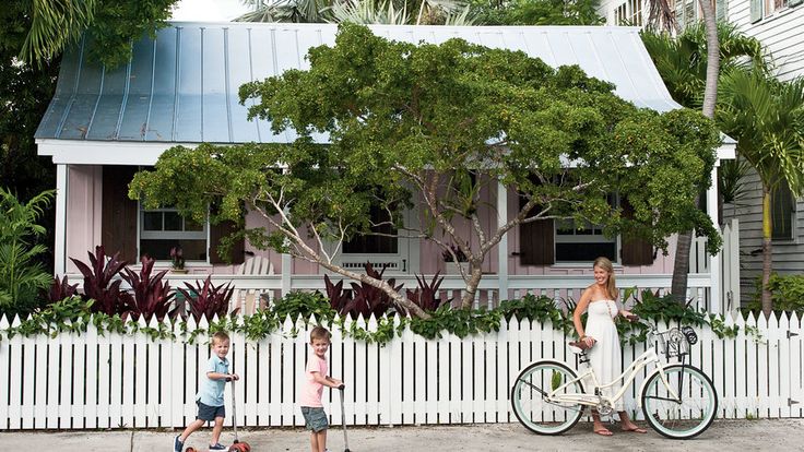 a woman and two children walking by a white picket fence with a bicycle in front of them