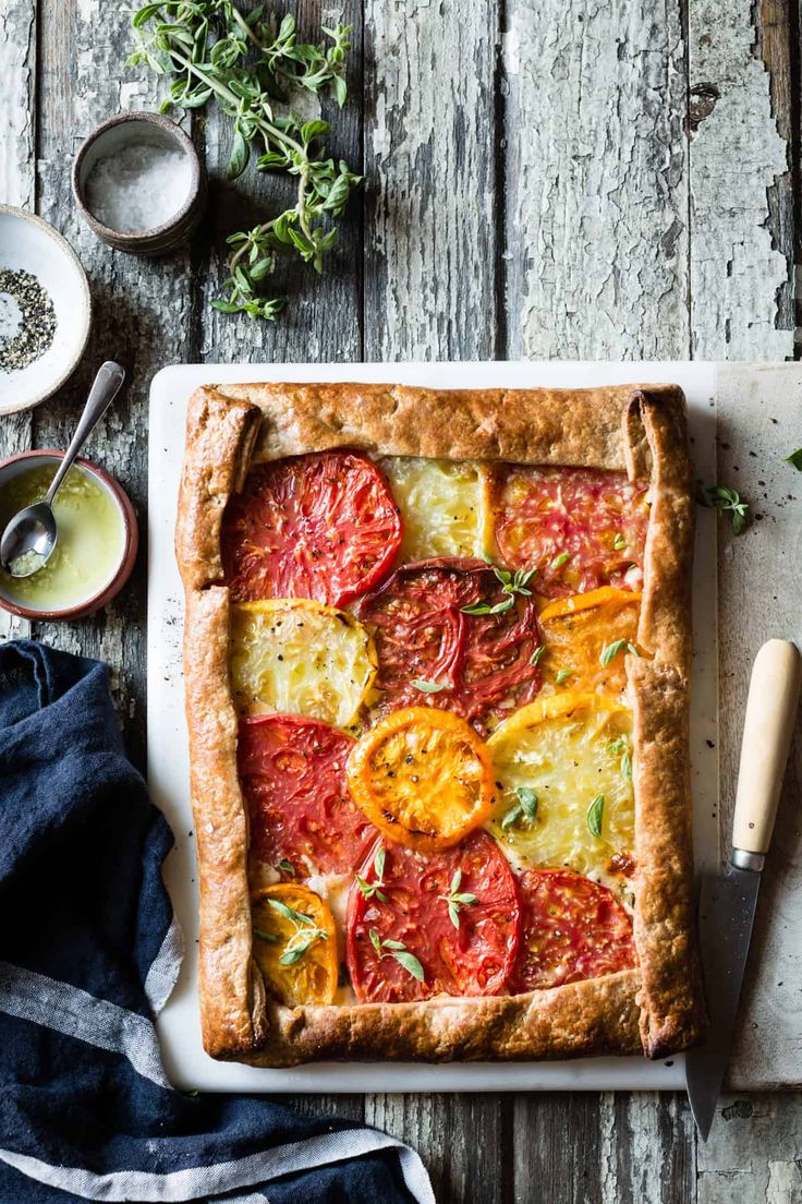 a tomato and cheese tart on a cutting board next to a knife, fork and spoon