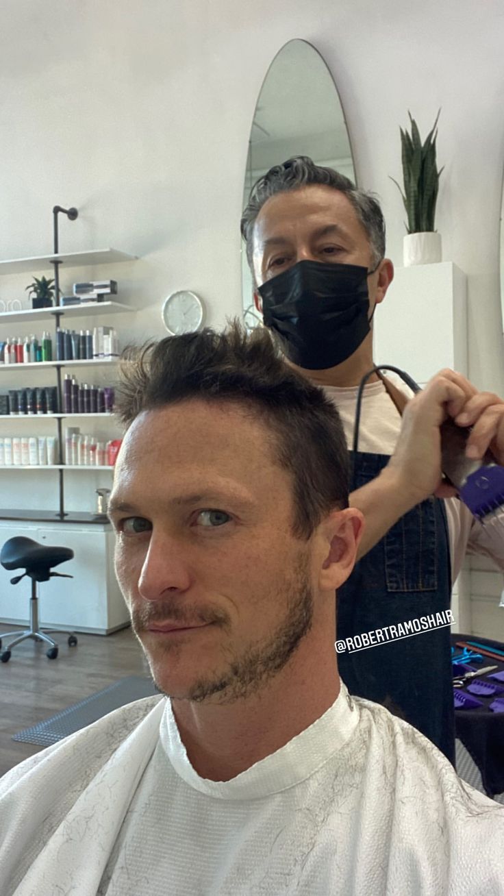 a man is getting his hair cut by another man in a barbershop wearing a face mask