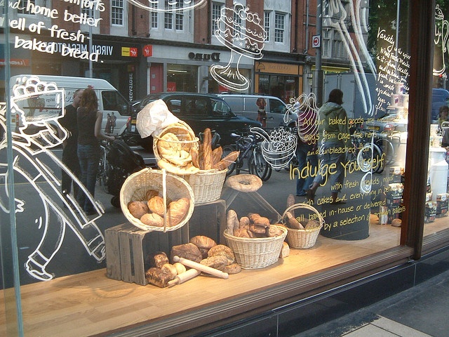 a bakery shop window with bread and pastries in baskets on the windows sill