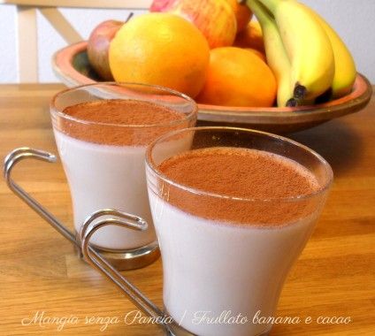 two glasses filled with chocolate drink next to bananas and oranges on a wooden table