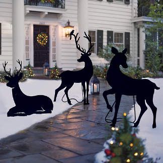 three metal reindeers with sleigh in front of a white house at christmas time