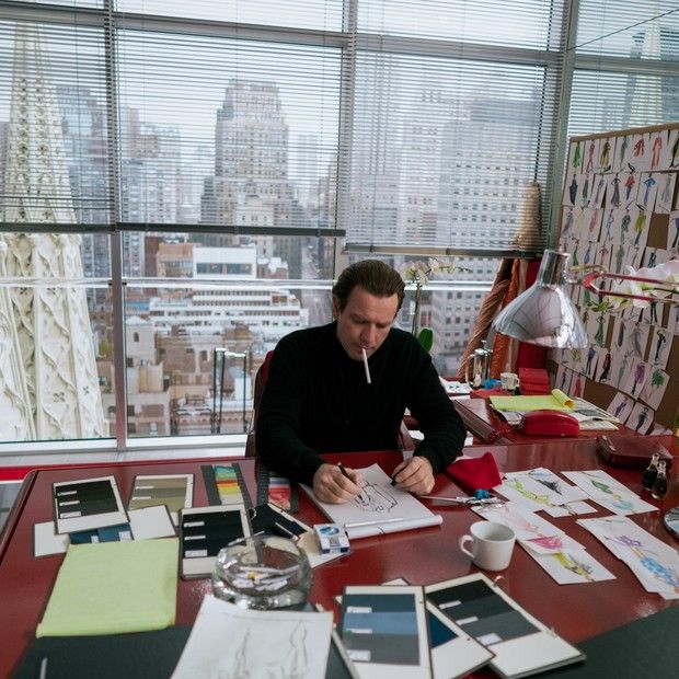 a man sitting at a desk with papers and pens in front of him, looking out the window