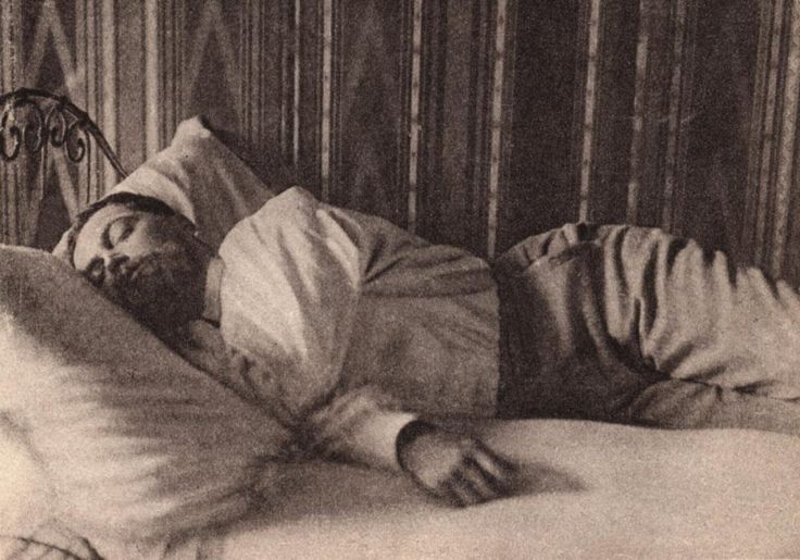 an old black and white photo of a man laying in bed with his head on the pillow