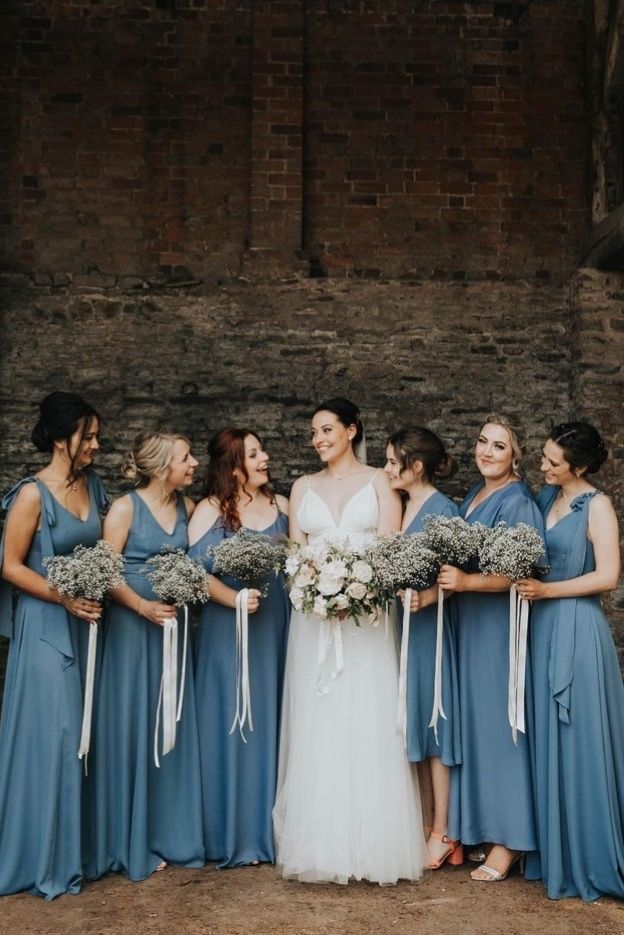 a group of women standing next to each other in front of a brick wall holding bouquets