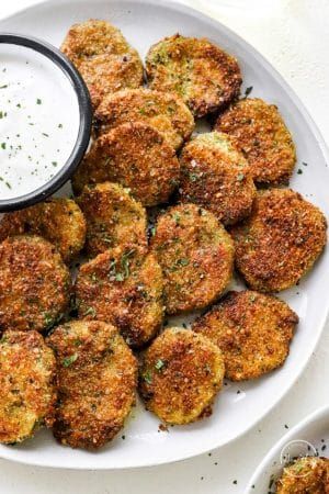 a white plate topped with crab cakes next to a small bowl of ranch dressing on the side