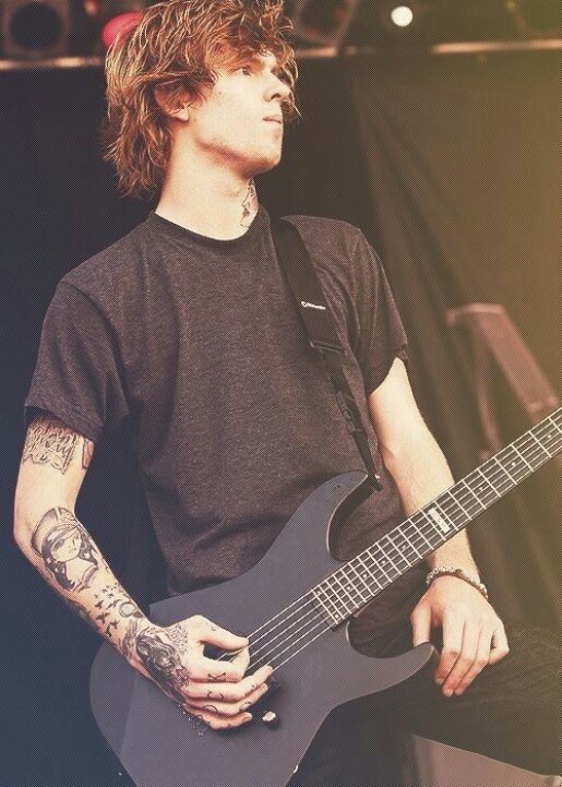 a man with long hair and tattoos playing a guitar in front of a microphone on stage