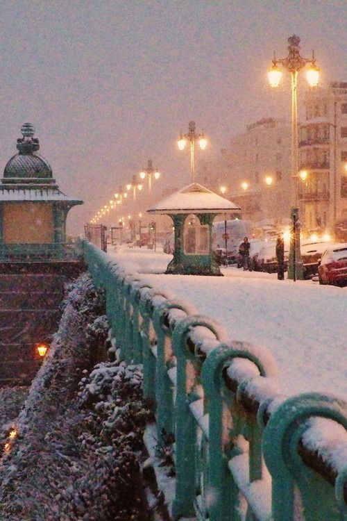 a snowy city street with cars parked on the side and people walking in the distance