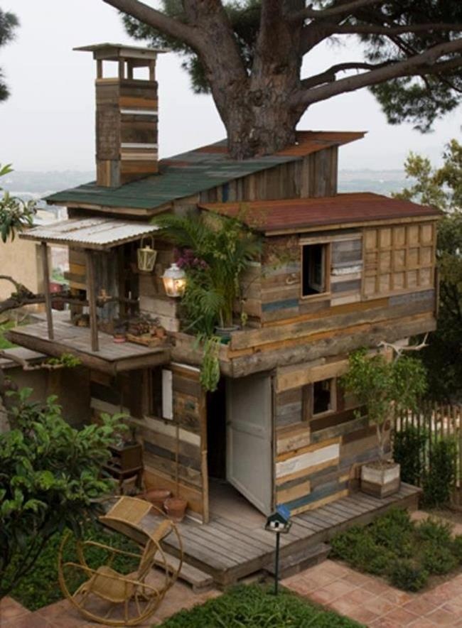 an old wooden house built into the side of a tree with lots of greenery