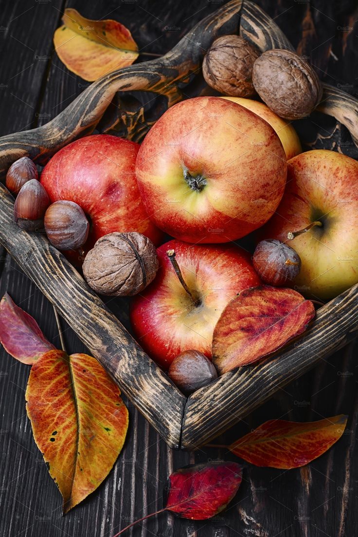 apples, nuts and leaves in a basket on a wooden table