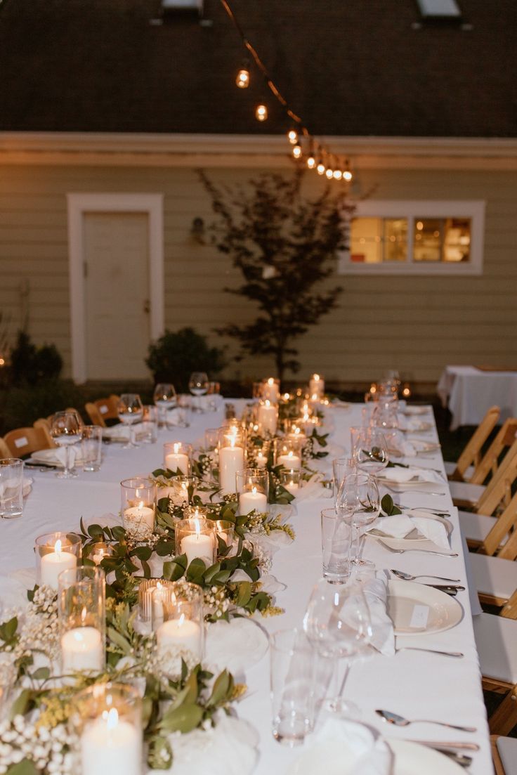 a long table is set with candles and greenery for an outdoor dinner party in the evening