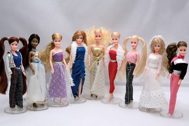 a group of barbie dolls standing next to each other on a white surface with one doll in the middle