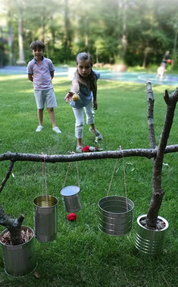 two children playing with tin cans on a tree branch in the grass, and one child is holding an apple