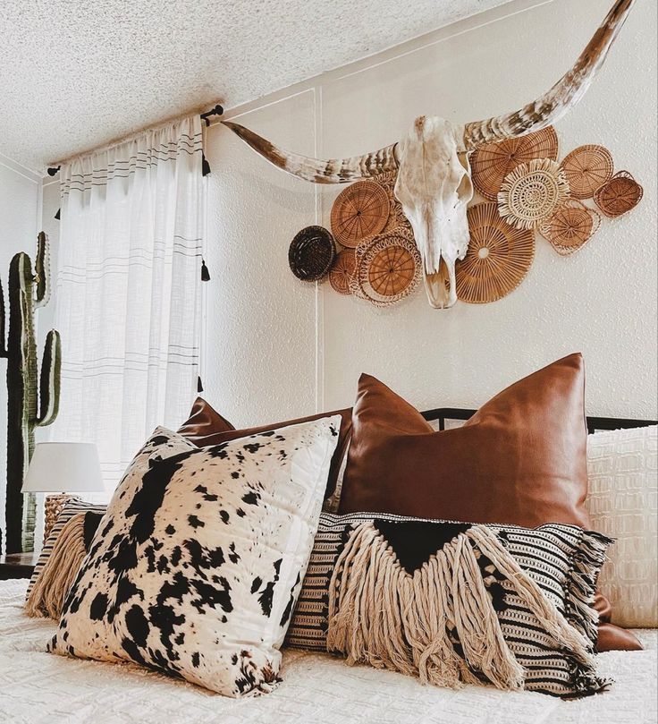 a bed topped with lots of pillows next to a wall mounted cow skull on the wall