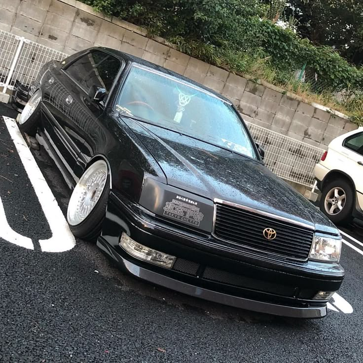 a black car parked in a parking lot next to a fence