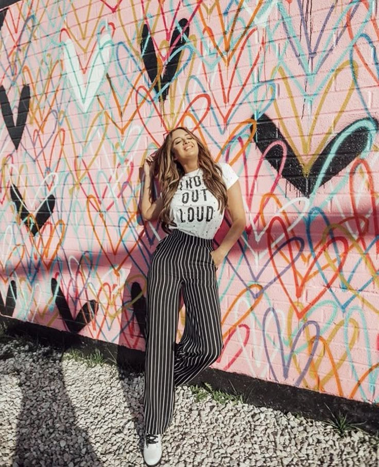 a woman standing in front of a wall with graffiti on it and her hands behind her head