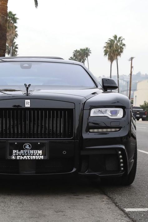 the front end of a black rolls royce parked on the side of the road with palm trees in the background