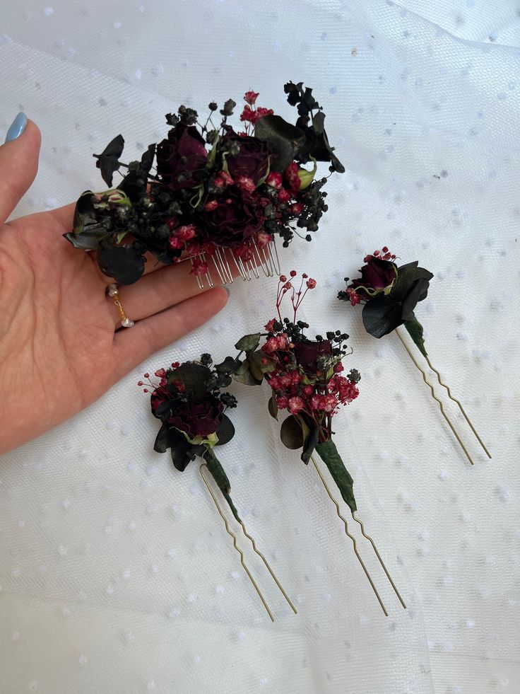 a hand is holding some flowers and hair pins