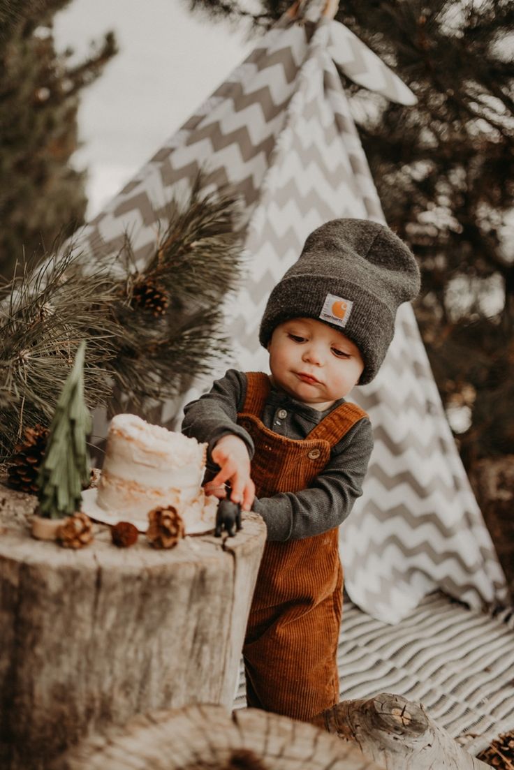 a small child standing next to a tree stump with a cake in front of him