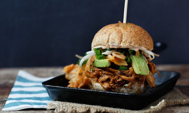 a pulled pork sandwich with avocado and slaw on a black plate next to a blue striped napkin