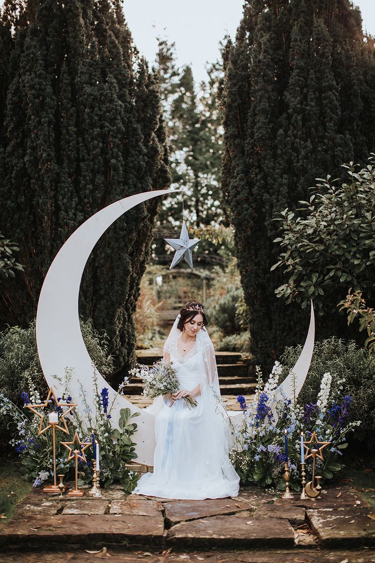 a woman in a wedding dress sitting on the moon with flowers and greenery around her