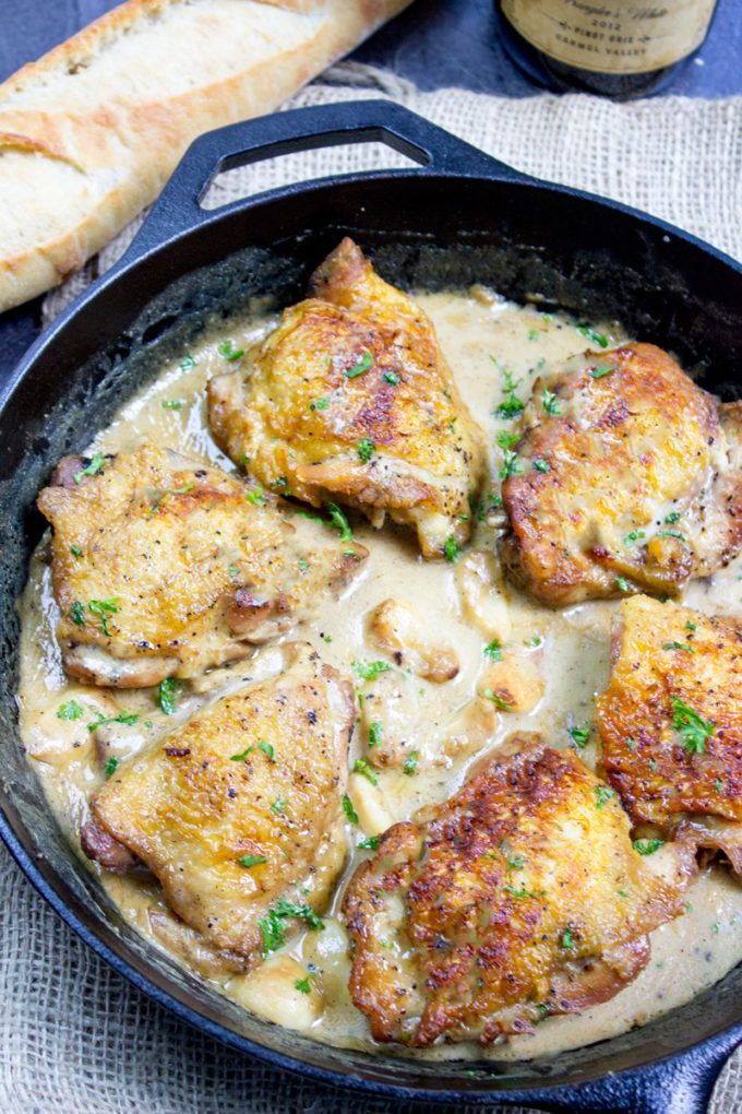 chicken with gravy in a cast iron skillet next to bread and wine