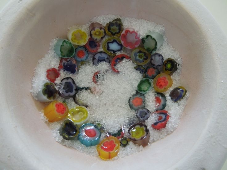 a bowl filled with lots of different colored glass beads on top of a white counter