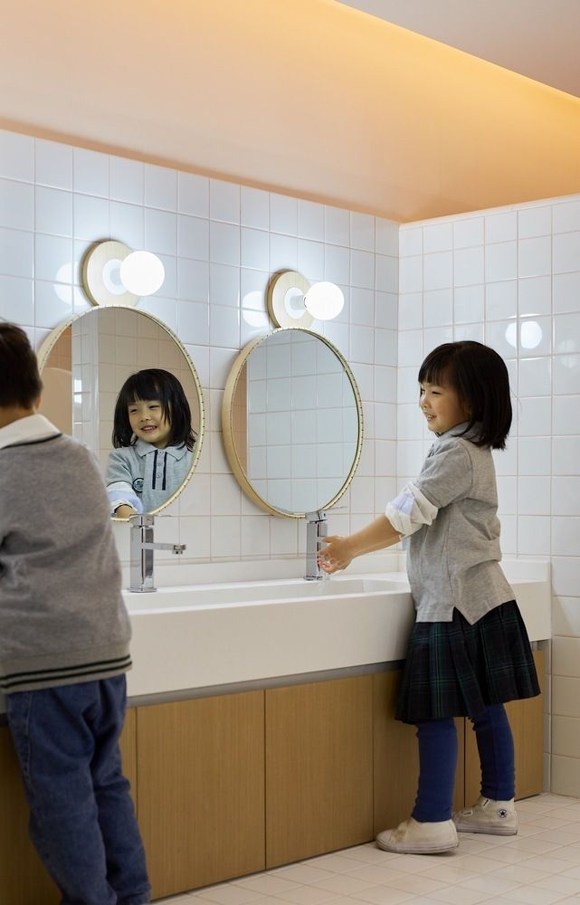 two young children standing in front of a bathroom sink with mirrors on the wall above them