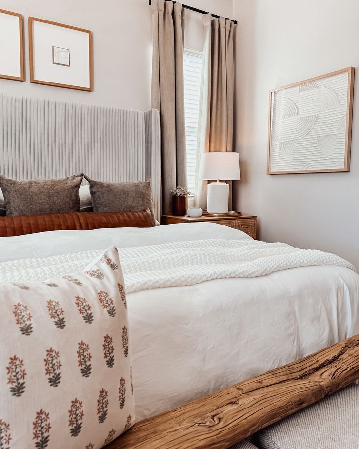 a bed with white sheets and pillows in a bedroom next to two framed pictures on the wall