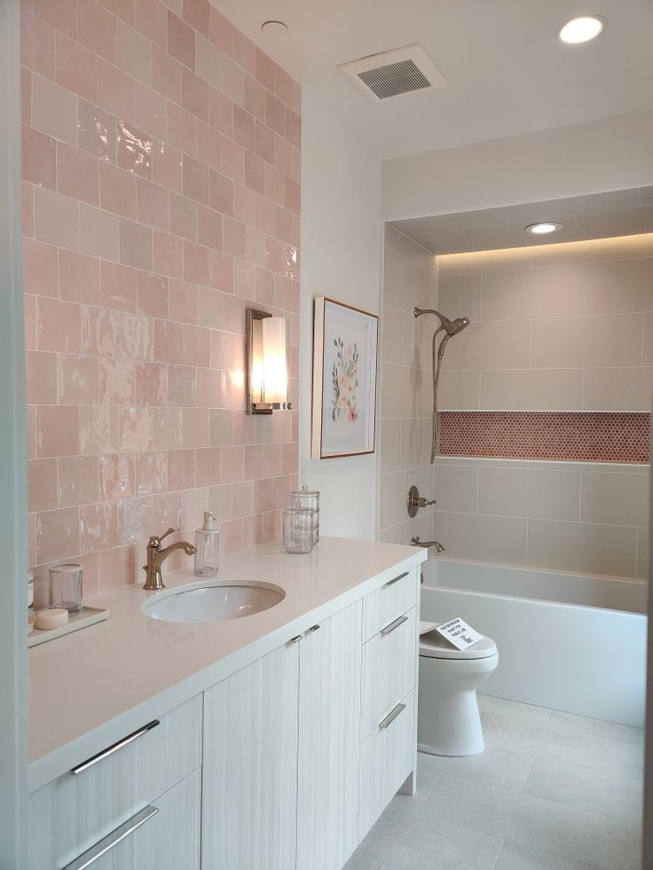 a bathroom with pink tiles on the walls and white cabinets, along with a toilet