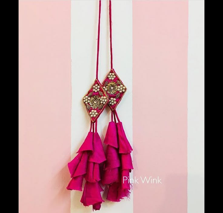 a pink wall hanging with two tassels on it's sides and a gold beaded design