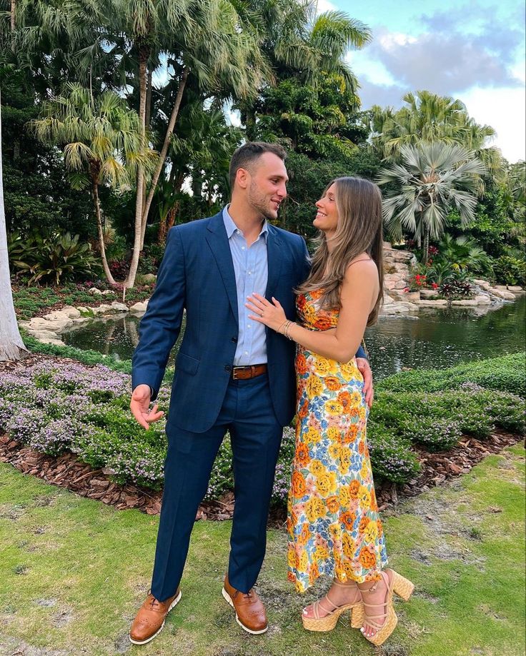 a man and woman standing next to each other in front of a pond with palm trees