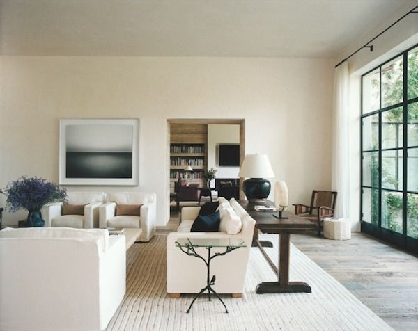 a living room with white furniture and large windows on the wall, in front of an open floor plan