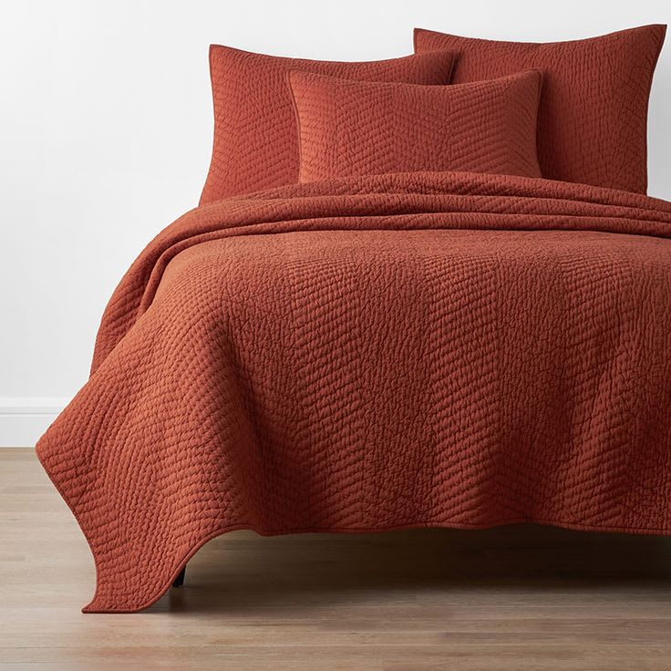 an orange quilted bedspread and pillows on a bed in a room with hardwood floors