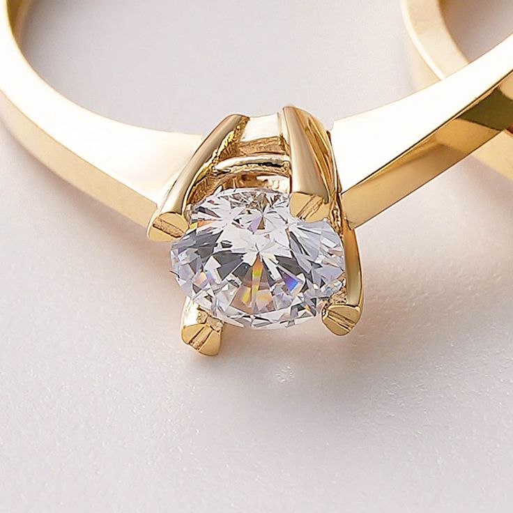 a gold ring with a white diamond in the center on a white surface, close up