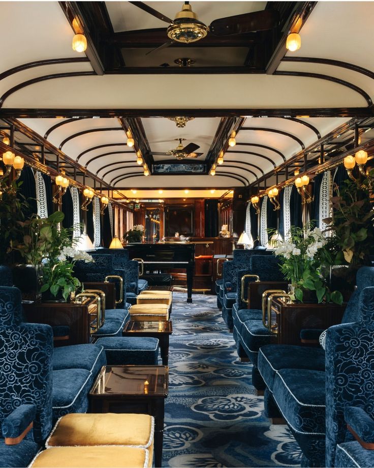 the inside of a train car with blue couches and tables on each side, along with potted plants