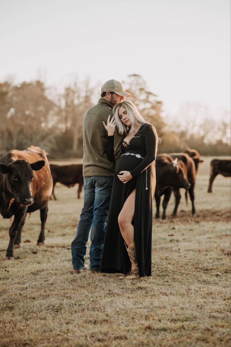 a man and woman standing next to each other in front of cows on a field