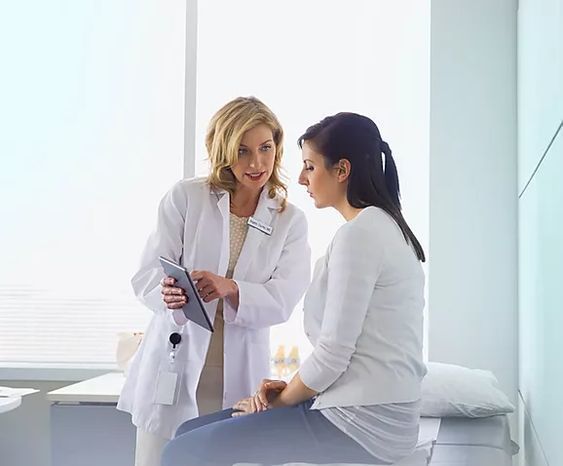 two women in white coats are talking to each other while sitting on a bed together