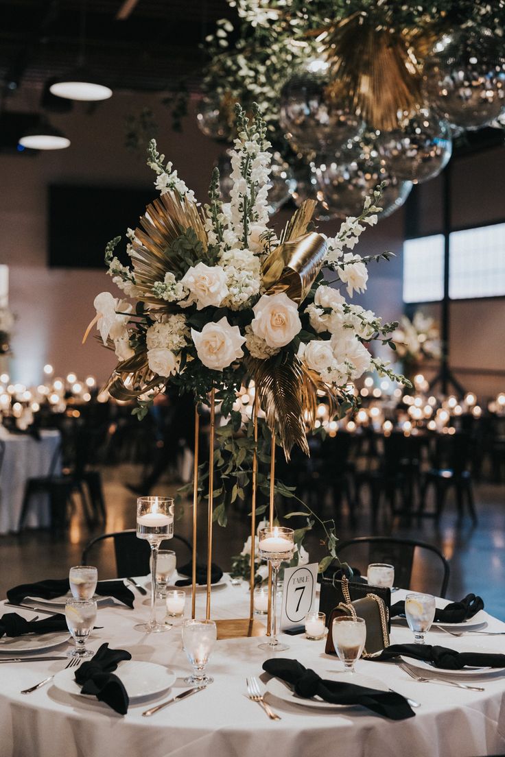 an elegant centerpiece with white flowers and greenery sits on a round table surrounded by black napkins