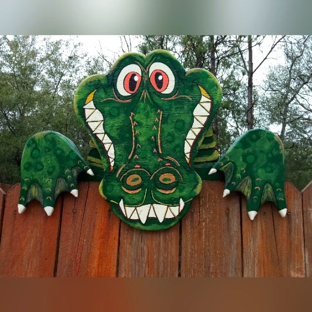 a green and white alligator head on top of a wooden fence