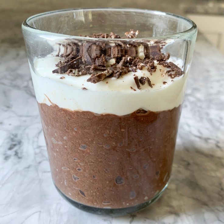 a dessert in a glass on top of a marble counter with white frosting and chocolate shavings