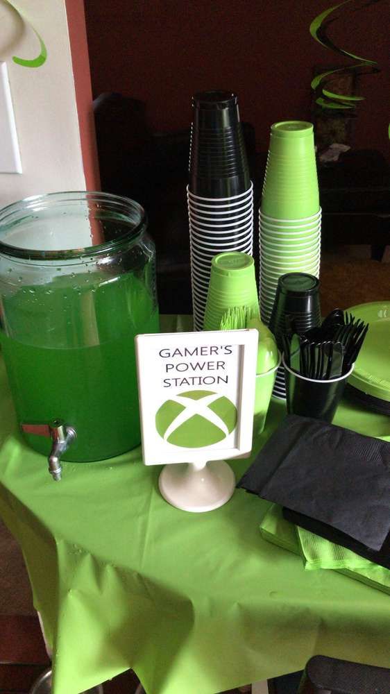 a table topped with green cups and plates next to a drink dispenser