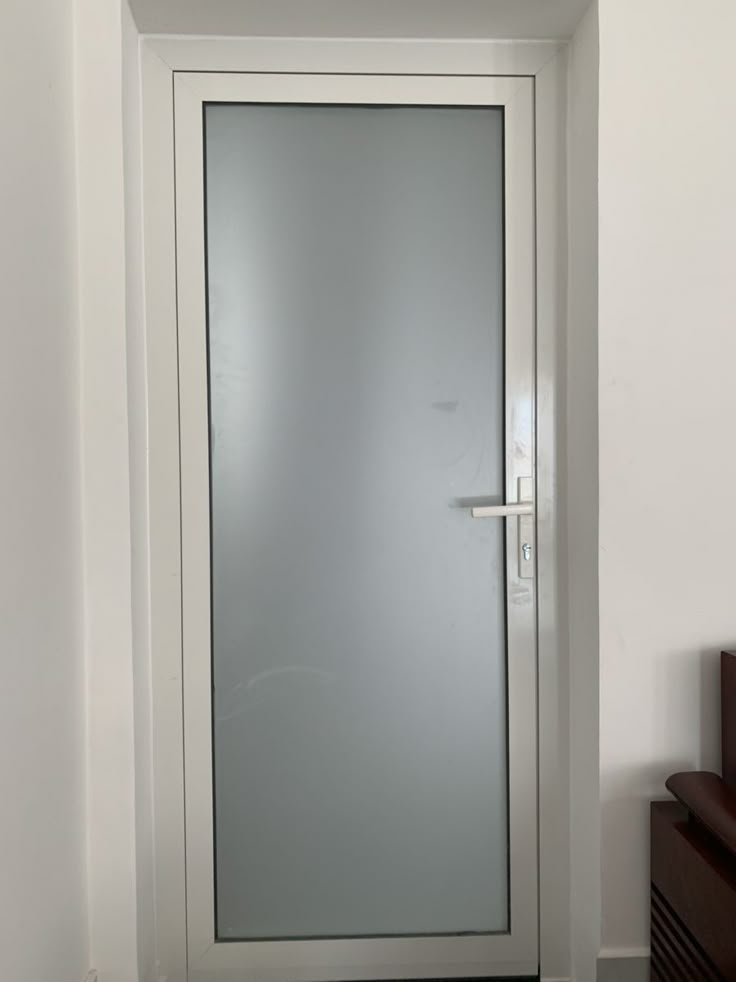 an empty room with a white door and brown chair in front of the door that has frosted glass on it