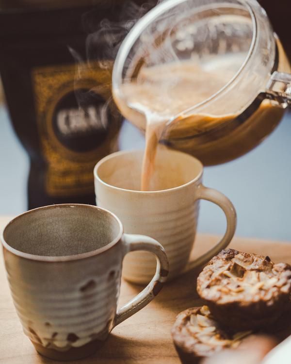 coffee being poured into two mugs with pastries next to them on a table