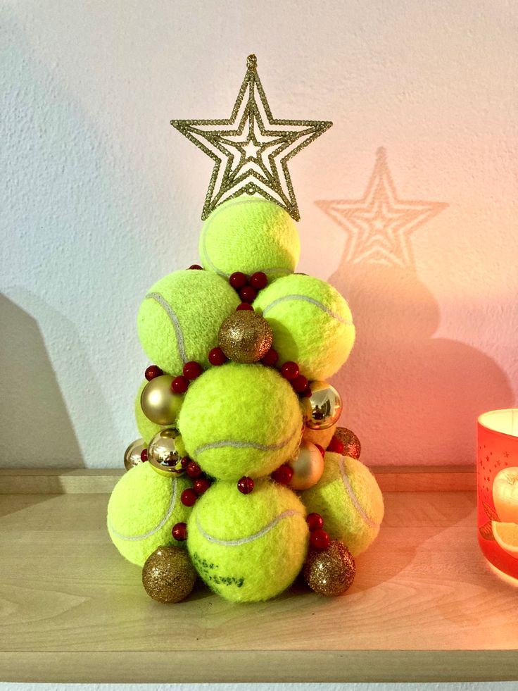 a christmas tree made out of tennis balls on a shelf next to a lit candle