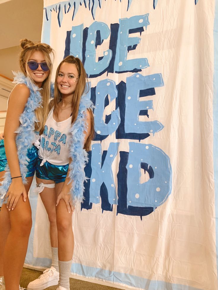 two girls in cheerleader outfits standing next to a banner